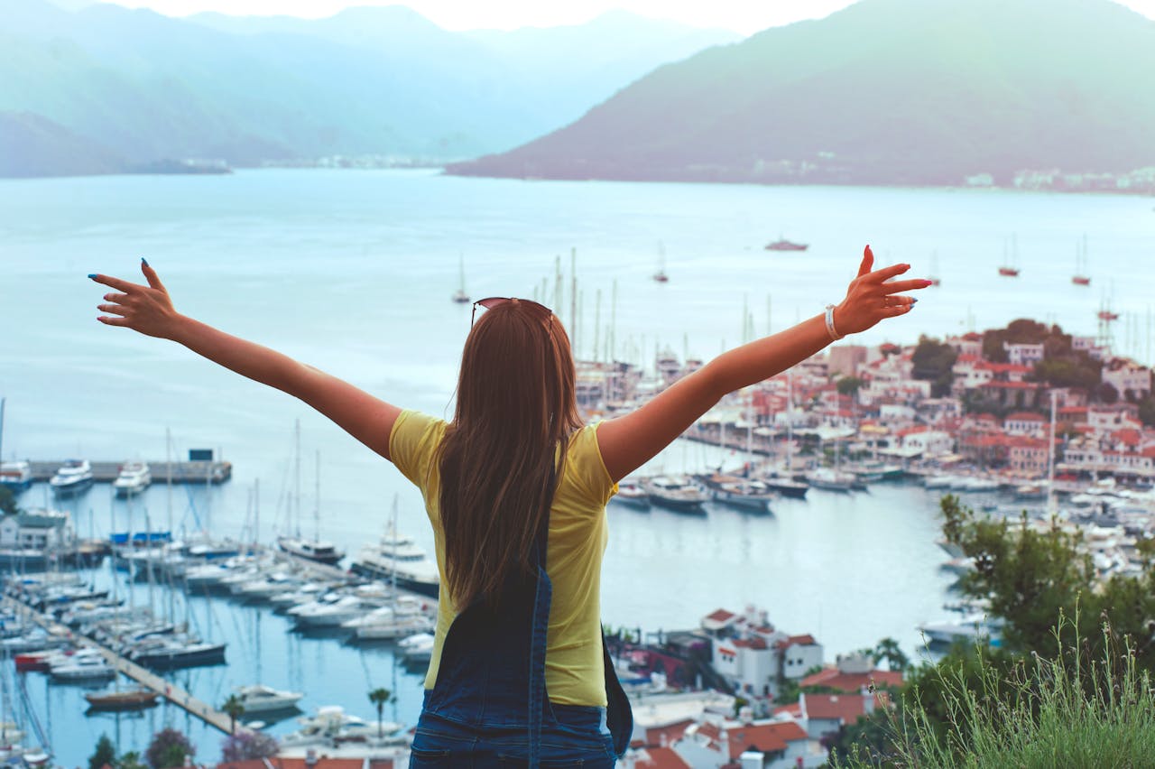our-mission A woman with open arms enjoys a scenic summer view of Marmaris harbor and yachts.