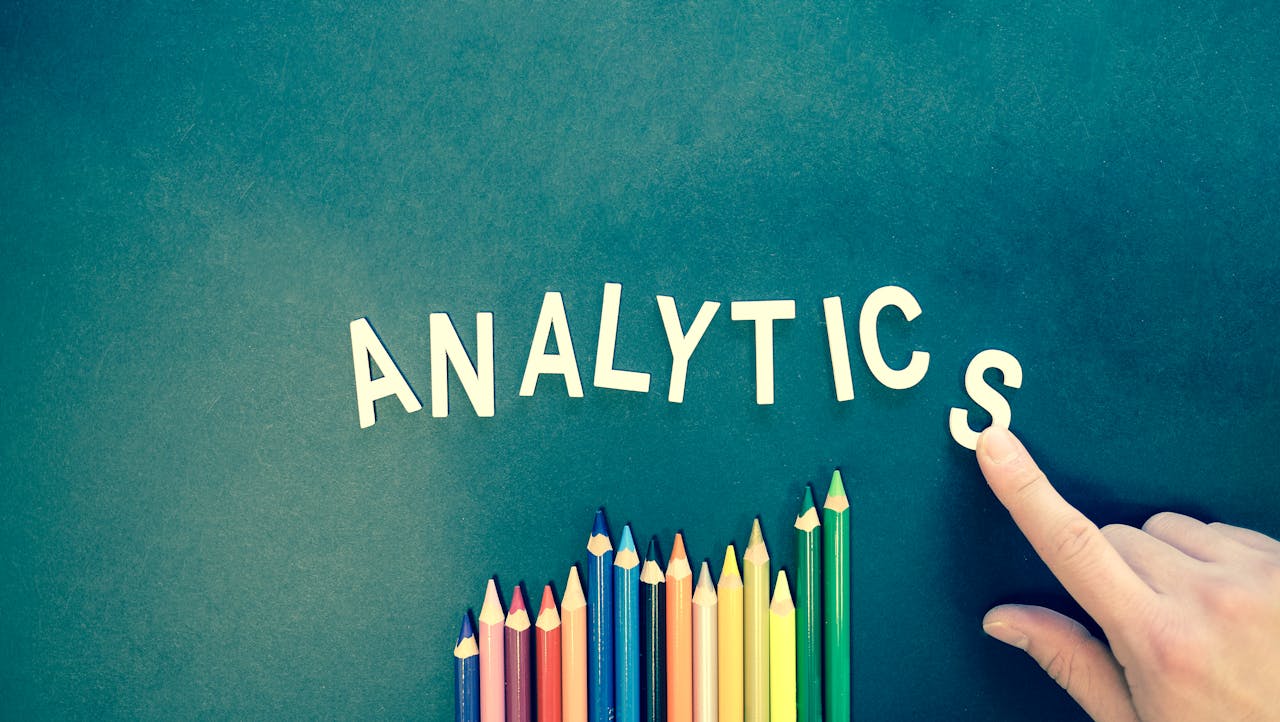 service-04 Colored pencils and letters spelling 'ANALYTICS' on a textured background with a hand.